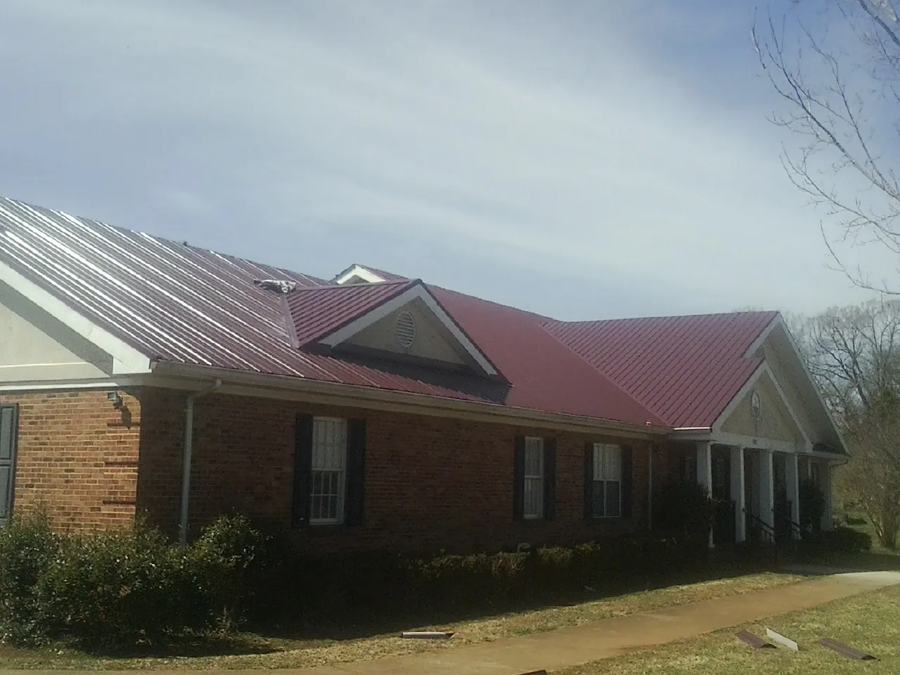 Red metal roof with gabled entries on a long brick building, from a Hail Damage Roof Repair job in Dundas